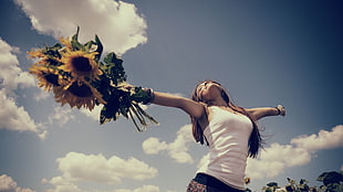 woman holding Sunflower bouquet spreading arms white standing under calm sky