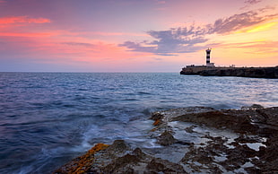photography of a sea with red and white lighthouse during sunset