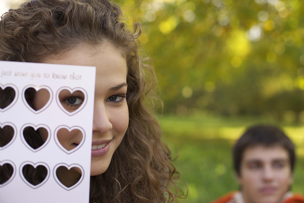 selective focus photography of woman looking through paper with heart hole HD wallpaper