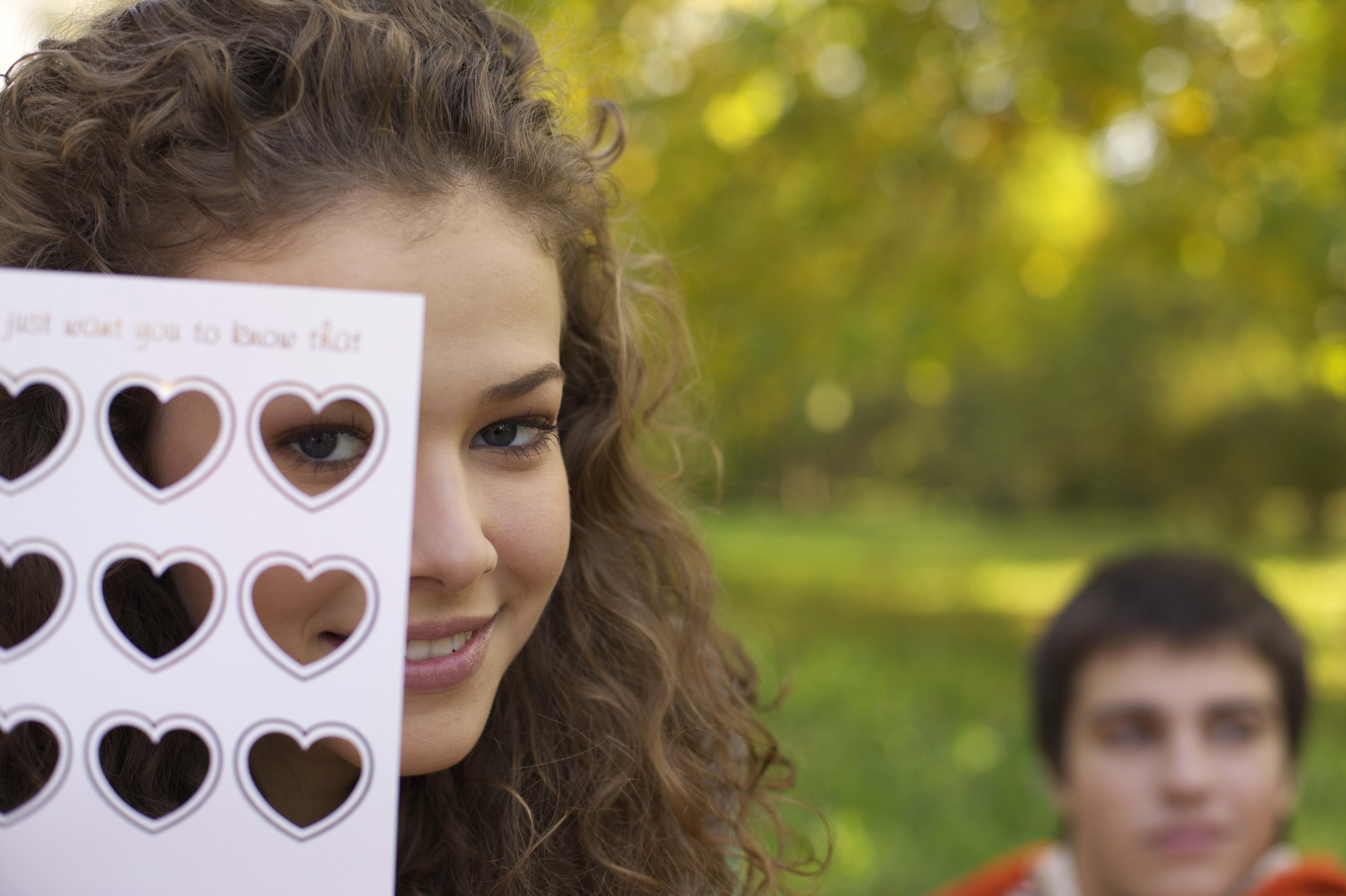 selective focus photography of woman looking through paper with heart hole