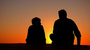 silhouette of man and boy sitting on ground with yellow background