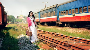 woman carrying suitcase standing beside train railway
