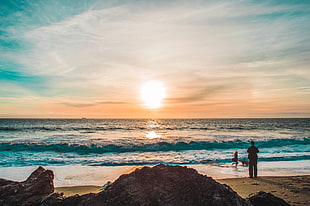 person standing on seashore during golden hour
