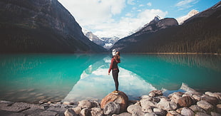 person standing on rock in front of the body of water and mountains, nature, water, trees, snow