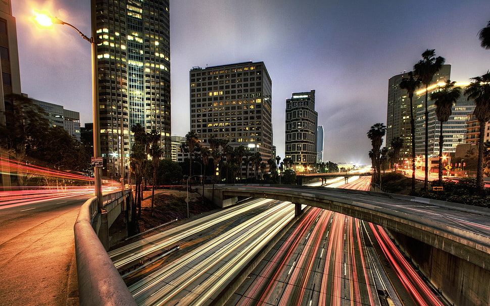 Time-lapse photography of roads between high-rise building during nighttime HD wallpaper