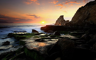 brown mountain near on the sea during sunset