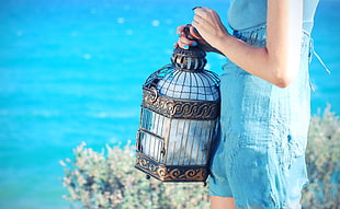 woman in blue sleeveless dress holding brown birdcage