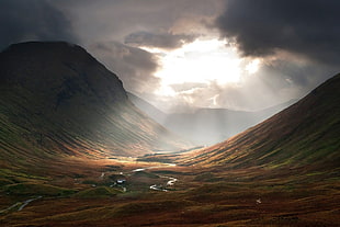 sunlight filtered through dark clouds on brown mountain landscape HD wallpaper