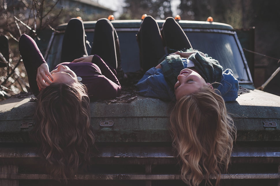 two girl's lying on car hood during daytime HD wallpaper