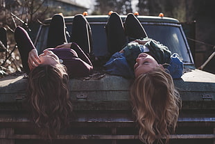 two girl's lying on car hood during daytime