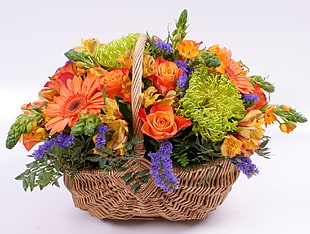 brown wicker basket with orange Rose and Daisy, purple Statice flowers, and green Spider Mum flowers
