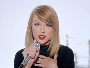 Taylor Swift in black turtle neck shirt holding microphone in hand