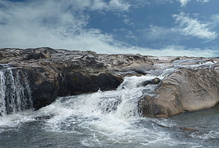 gray rock formation with flowing water under the clear blue skies