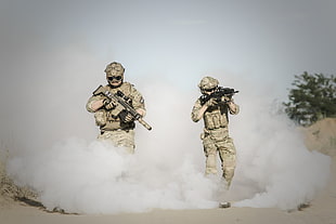 photo of two men holding riffle surrounded by smoke in the dessert