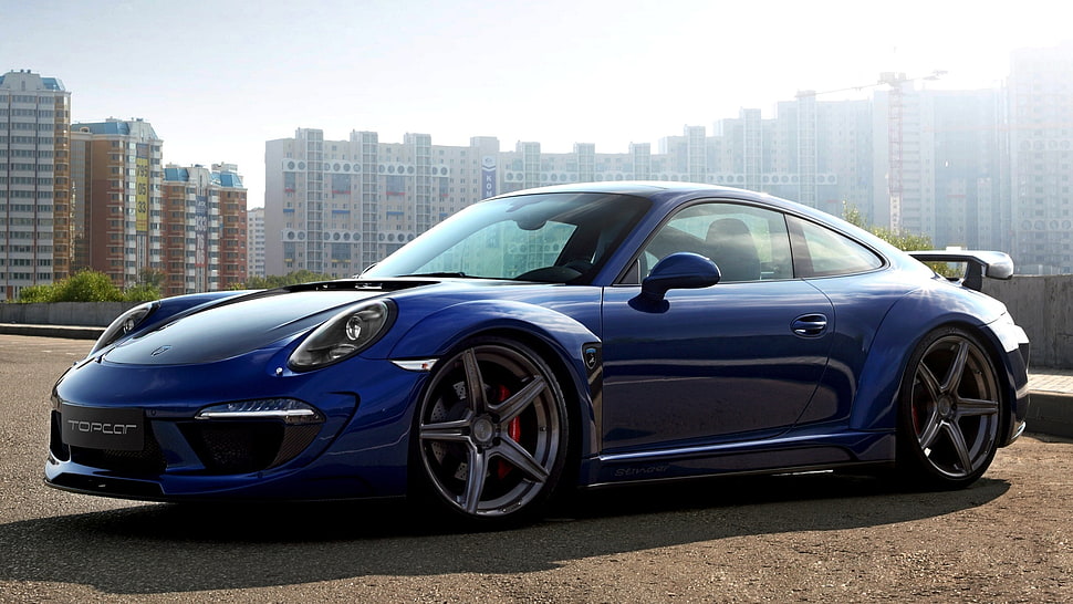 blue Porsche 911 parked on brown soil with view of high-rise building HD wallpaper