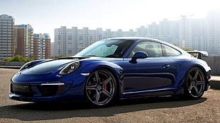 blue Porsche 911 parked on brown soil with view of high-rise building