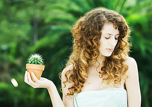 selective focus photography of a naked woman holding Cactus plants with brown pot with closing her eyes