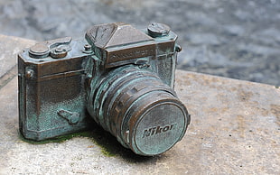 brown and teal Nikon DSLR camera miniature on brown concrete surface