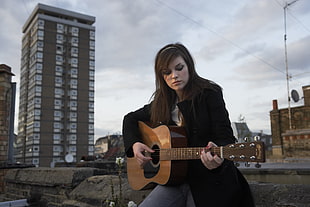 woman playing acoustic guitar at the city during day