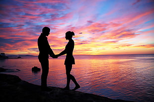 couple facing each other on seashore during sunset