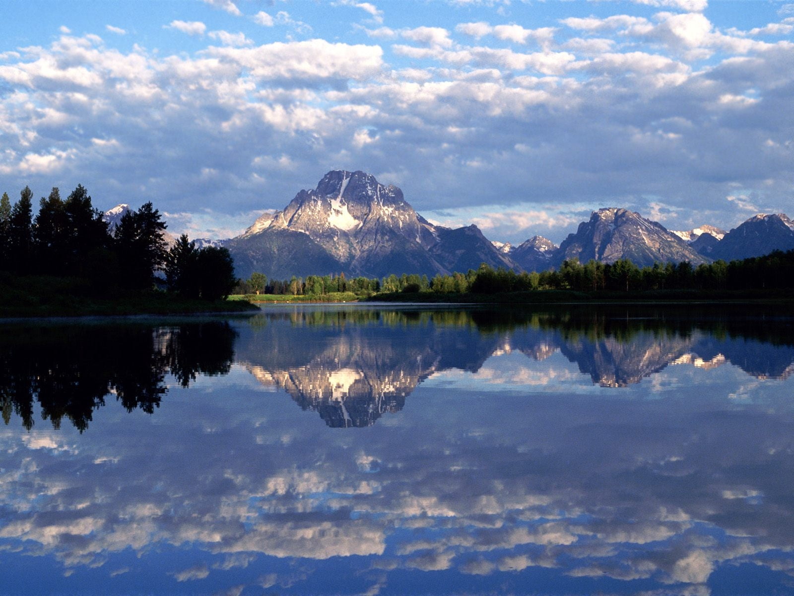 mountain in distance with body of water refection of mountain under cloudy sky at daytime