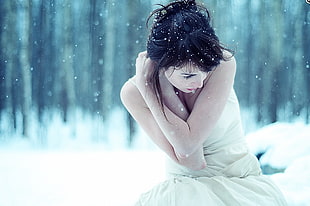 selective focus photography of woman wearing white pleated sleeveless dress sitting on snowy terrain