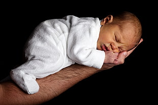 baby in white sleeper lying on mans right arm