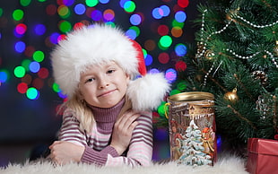 girl wearing pink striped sweater sitting near christmas tree and pose for picture