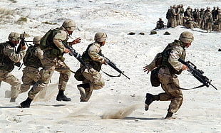 five soldiers running at desert while holding black assault rifles during daytime
