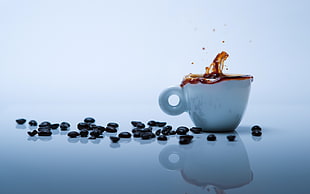 photo of white teacup filled with coffee beside spilled coffee beans