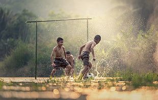 three boy playing soccer on green grass field