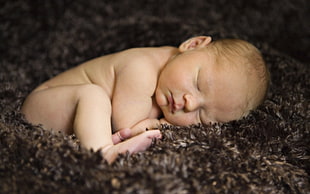 photo of baby sleeping on brown fleece cushion