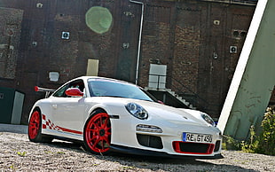 white and red Porsche 911 parked near brown concrete building at daytime