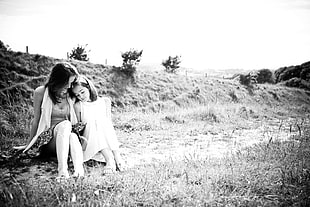 grayscale photo of woman beside girl sitting on grass field