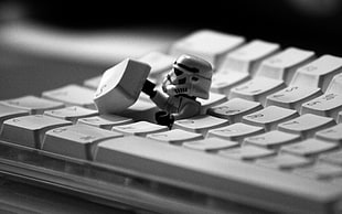 grayscale photography of stormtrooper plastic toy hiding in white computer keyboard