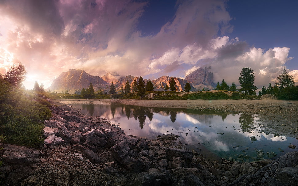 calm body of water near brown rocks, lake, sunset, mountains, clouds HD wallpaper