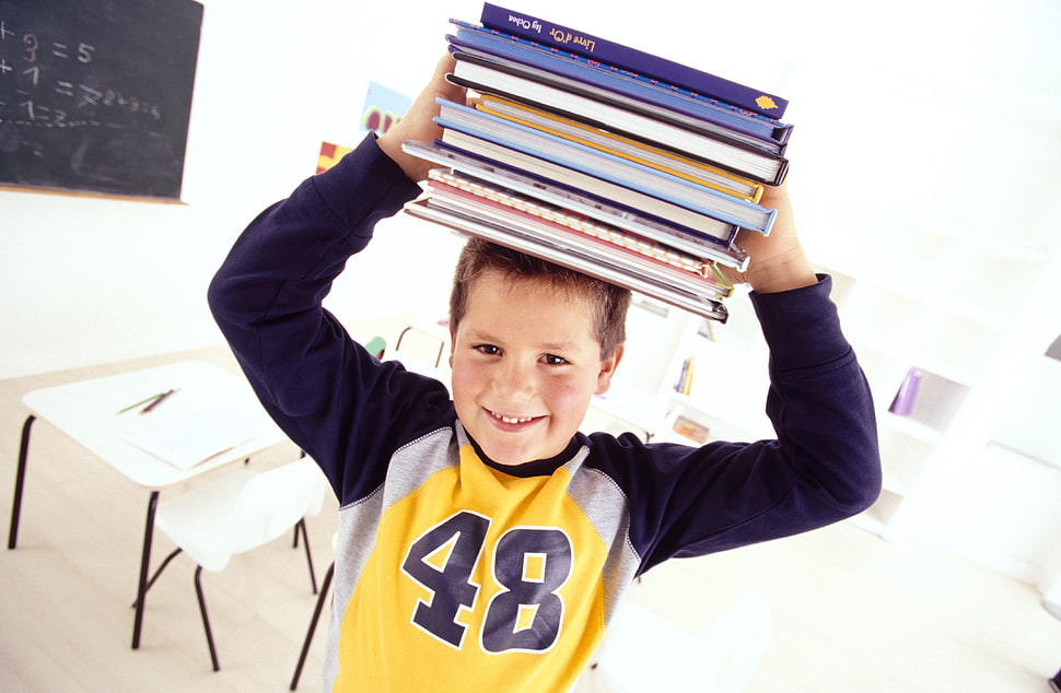 boy wearing yellow and blue long sleeve shirt lifting books HD wallpaper