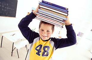 boy wearing yellow and blue long sleeve shirt lifting books