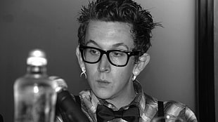 grayscale photo of man in dress shirt with bowtie and eyeglasses