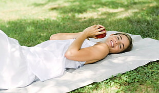 woman in white sleeveless dress lying on top of white textile and grass field
