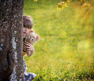 girl holding teddy bear hiding in brown and white tree trunk