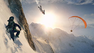 man in black suit near person diving on snow near man doing paragliding with parachute during daytime