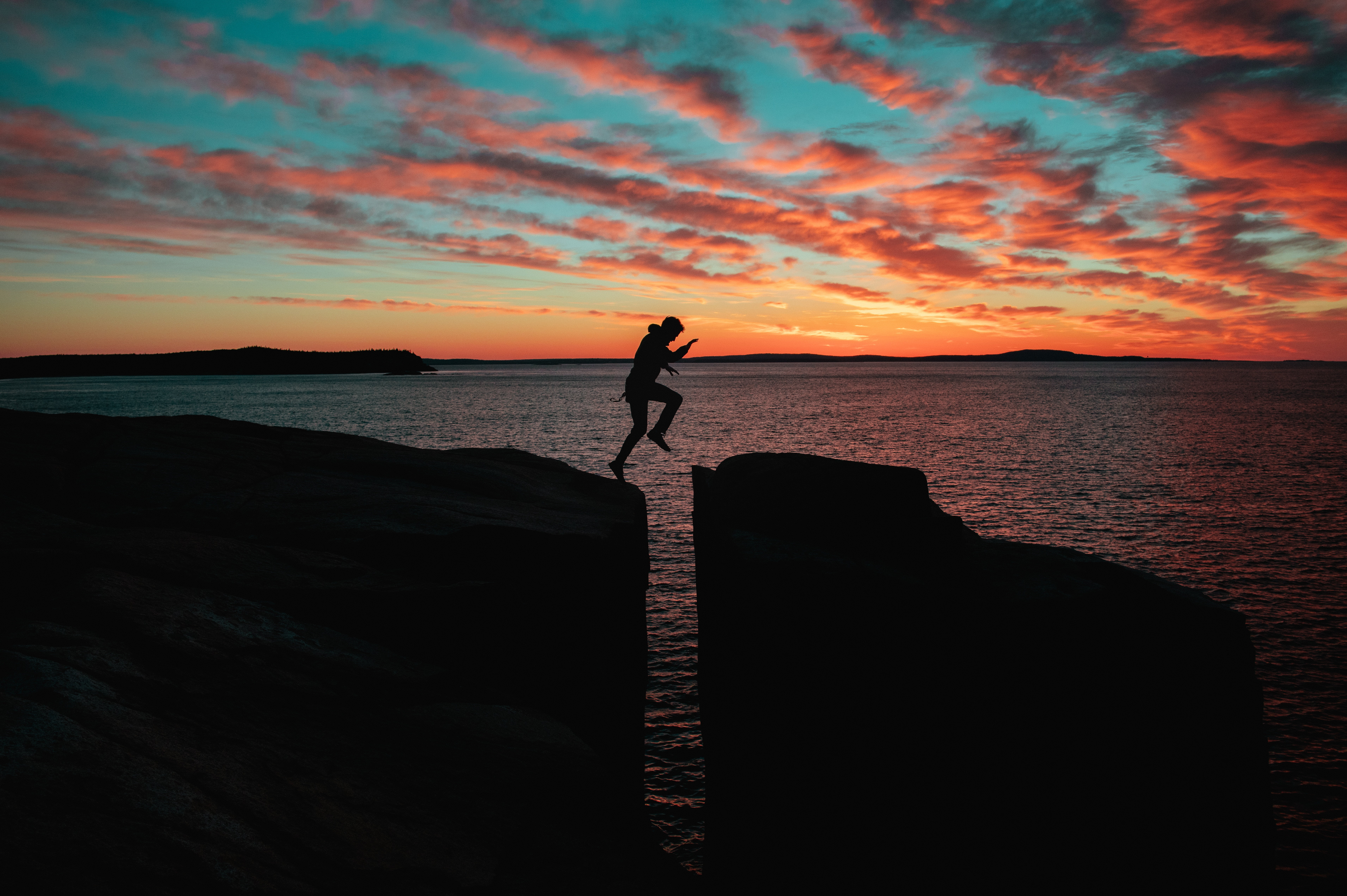 silhouette of man jumping over cliff