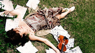 woman wearing red and gray tube dress holding violin on green grass at daytime