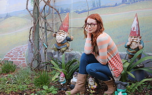 woman in brown and orange striped jacket sitting near gnome decors