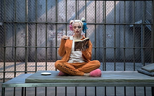 DC Suicide Squad Harley Quinn sitting inside gray metal cage while holding teacup and reading book movie scene