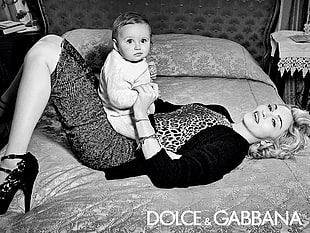 gray scale photography of woman laying on bed holding a baby