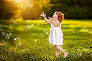 girl wearing white shirt playing with bubbles in green grass field