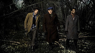 three men wearing overcoats and pants while walking in a forest