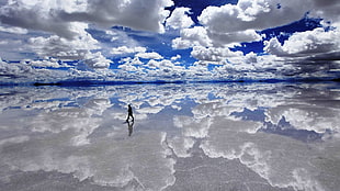 man walking of body of water under cloudy sky during daytime HD wallpaper